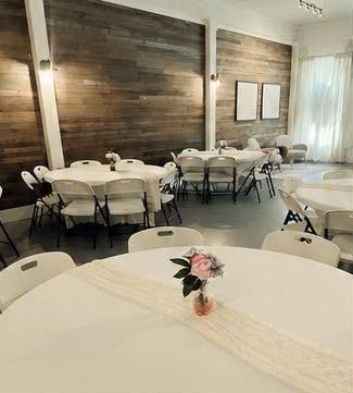Round tables with white linens and a floral centerpiece beside the wood-plank wall